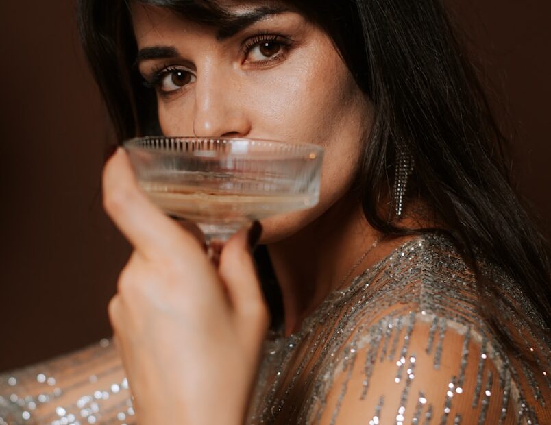 Woman in sparkling dress drinks from champagne glass